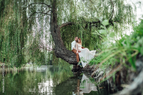 a guy and a girl are sitting together on a crooked tree on the steep bank