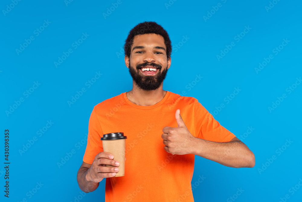 happy african american man showing thumb up and holding paper cup isolated on blue happy african american man showing thumb up and holding paper cup isolated on blue