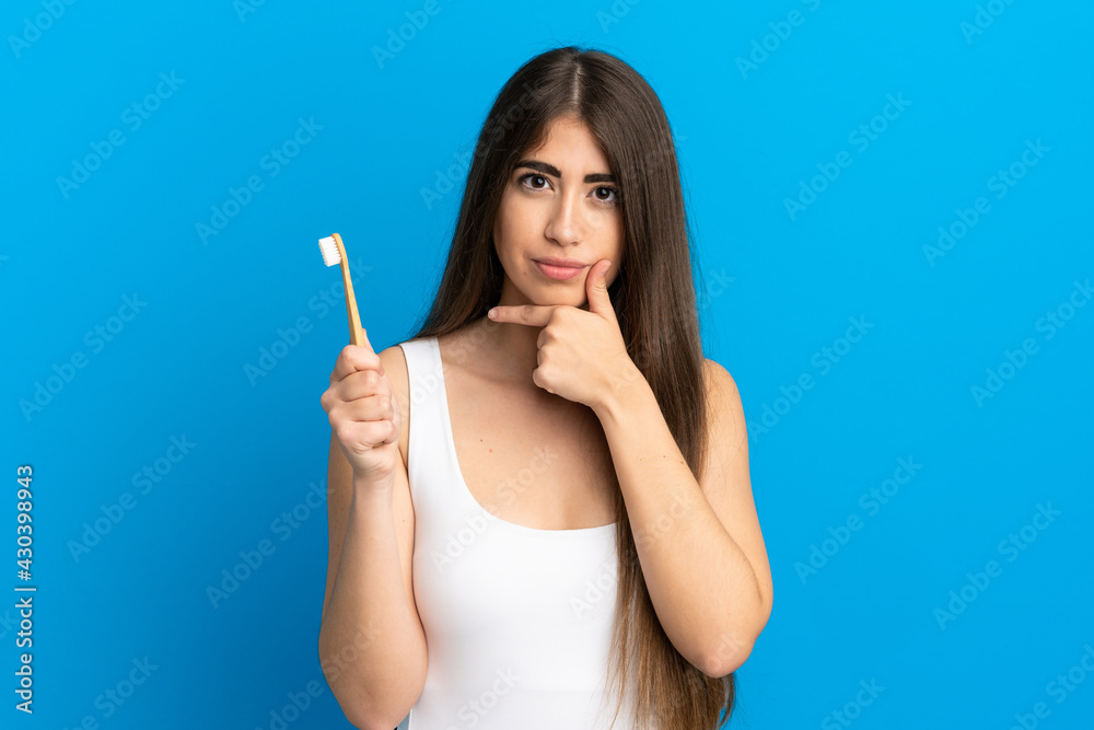 Young caucasian woman brushing teeth isolated on blue background thinking Young caucasian woman brushing teeth isolated on blue background thinking