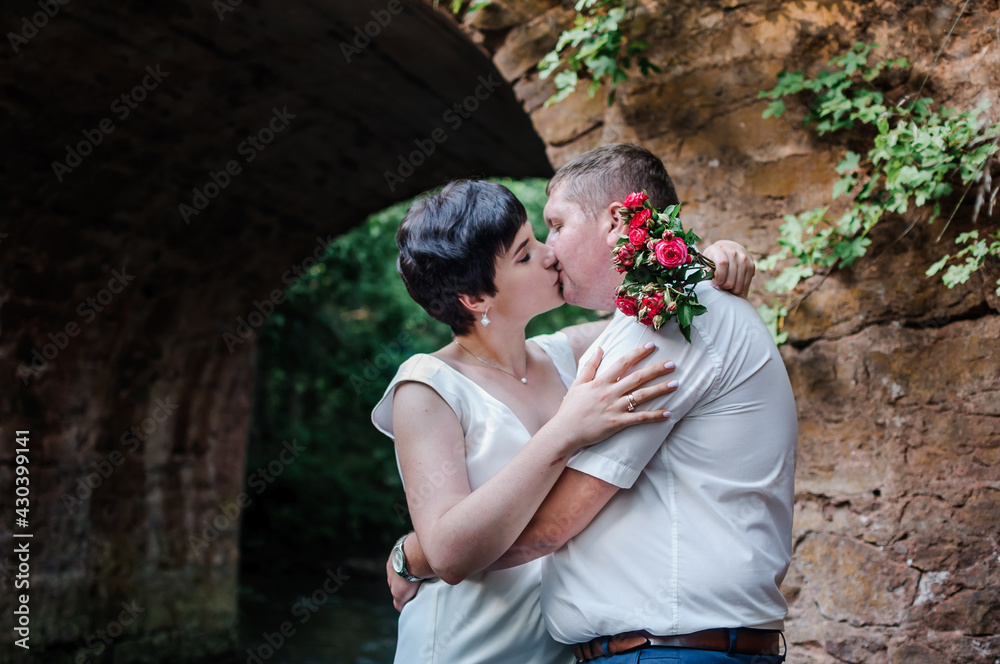 The bride and groom hug and kiss against the background of water and a stone arch