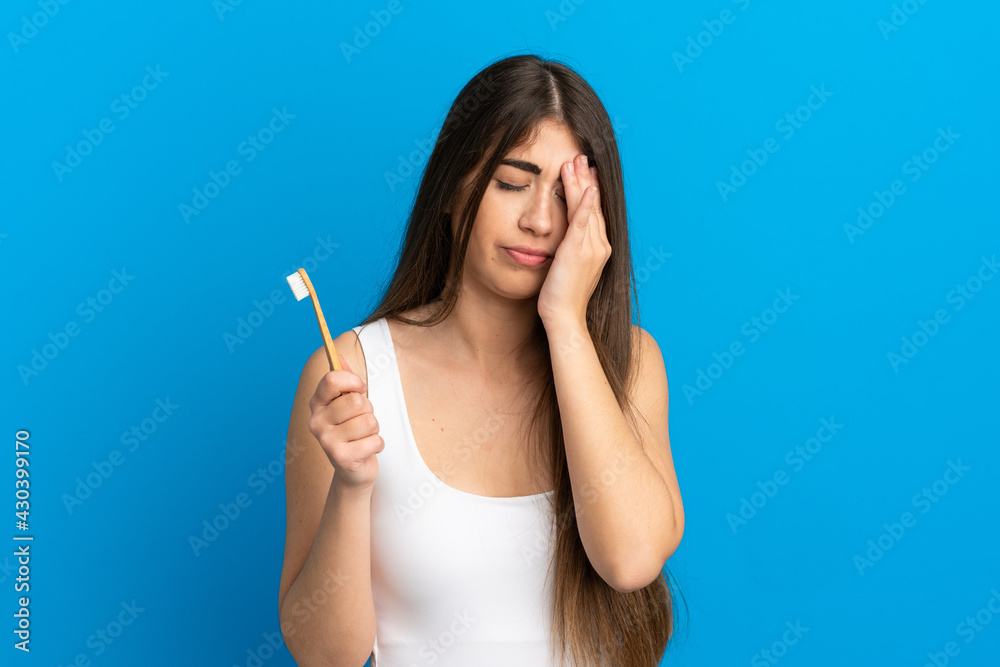 Young caucasian woman brushing teeth isolated on blue background with tired and sick expression Young caucasian woman brushing teeth isolated on blue background with tired and sick expression