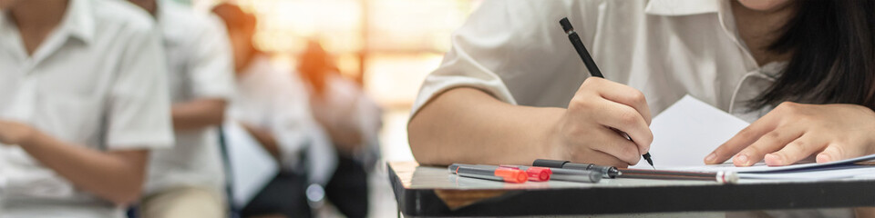 Exam at school with student's taking educational admission test in class, thinking hard, writing answer in university classroom, education and world literacy day concept