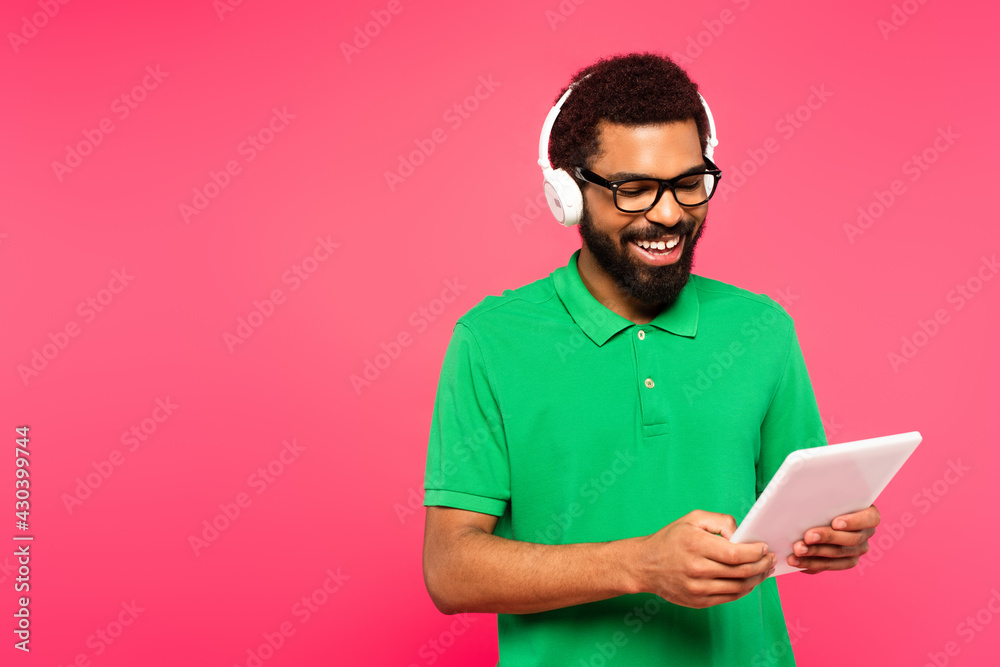 cheerful african american man in glasses and headphones using digital tablet isolated on pink cheerful african american man in glasses and headphones using digital tablet isolated on pink