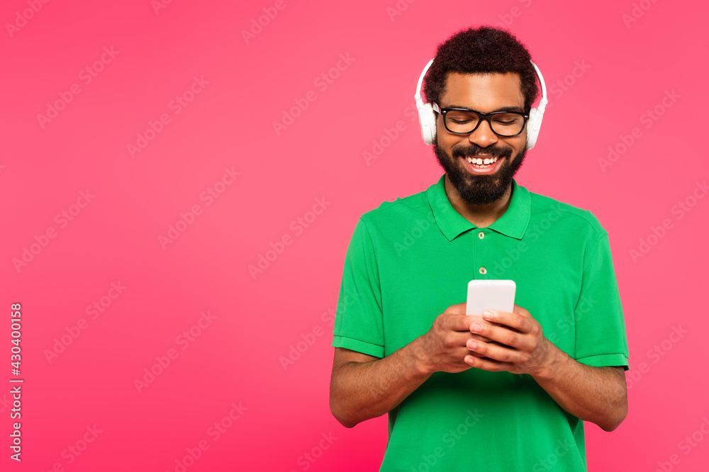 happy african american man in glasses and wireless headphones using smartphone on pink happy african american man in glasses and wireless headphones using smartphone on pink