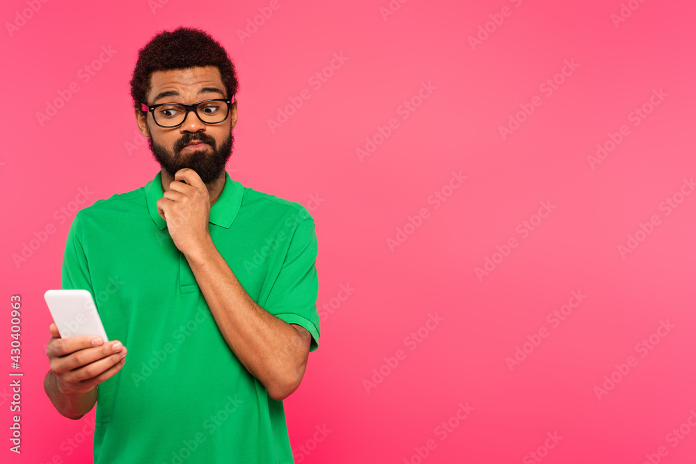 pensive african american man in green t-shirt using smartphone isolated on pink pensive african american man in green t-shirt using smartphone isolated on pink