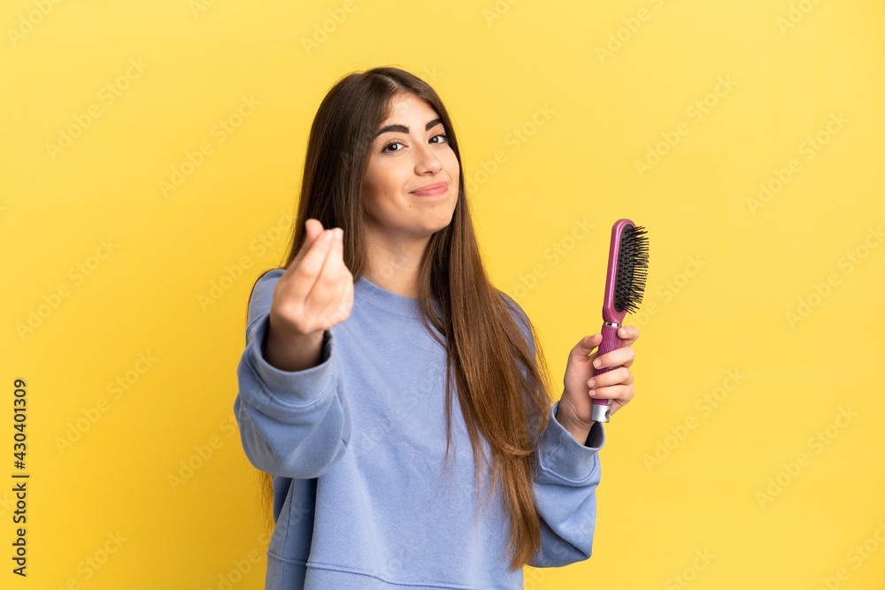 Young caucasian woman holding hairbrush isolated on blue background making money gesture Young caucasian woman holding hairbrush isolated on blue background making money gesture
