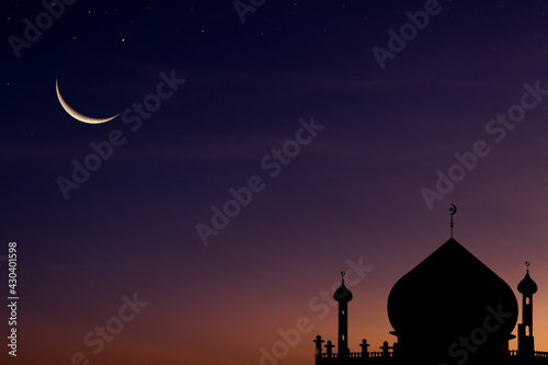 Crescent moon on dusk twilight sky over silhouette dome mosques, symbols of religious Islamic Ramadan month