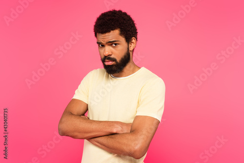 offended african american man standing with crossed arms isolated on pink