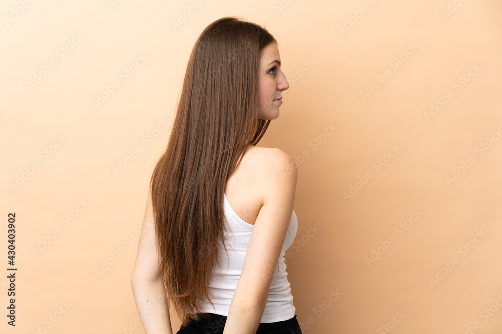 Young caucasian woman isolated on beige background in back position and looking back Young caucasian woman isolated on beige background in back position and looking back