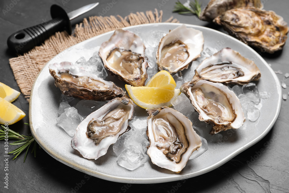 Delicious fresh oysters with lemon slices served on black slate table, closeup Delicious fresh oysters with lemon slices served on black slate table, closeup