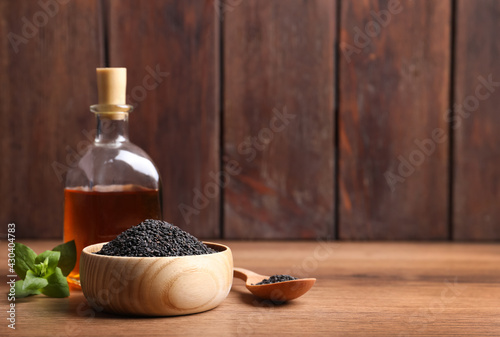 Black sesame seeds, oil and green leaf on wooden table, space for text photo