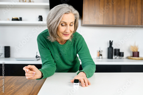 Technology for health screening at home. Senior woman using oximeter for measures the oxygen saturation in the blood, put device on finger and monitoring indicators photo