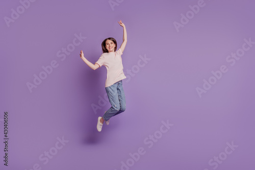 Portrait of funny positive girl jump raise hands on purple wall