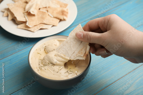 Woman dipping pita chip into hummus at turquoise wooden table, closeup