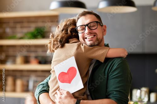 Φωτογραφία Little girl daughter congratulating dad with Fathers day or Birthday and giving him greeting postcard with red heart, happy man daddy embracing his child