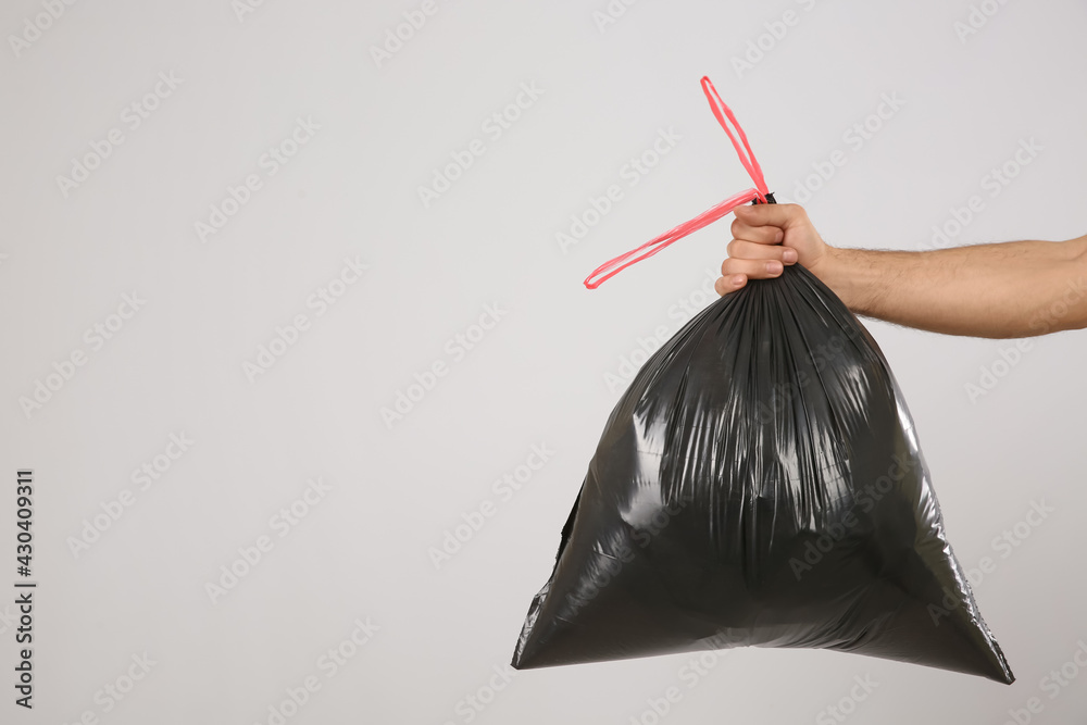 Man holding full garbage bag on light background, closeup. Space for text - obrazy, fototapety, plakaty 