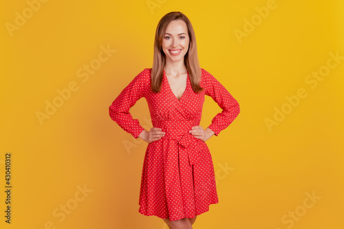 Close-up of a woman smiling hands hips wear red short dress on yellow wall