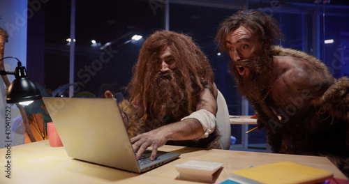 Primitive neanderthal people couple traveling through time working in contamporary office playing woith gagdets interacting new things.