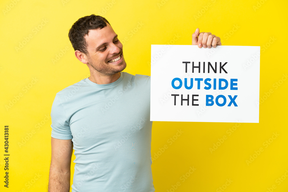Brazilian man over isolated purple background holding a placard with text Think Outside The Box Brazilian man over isolated purple background holding a placard with text Think Outside The Box