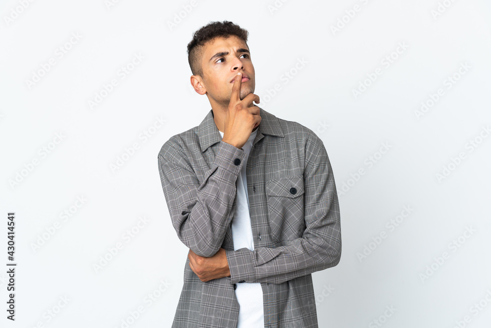 Young brazilian man isolated on white background having doubts while looking up