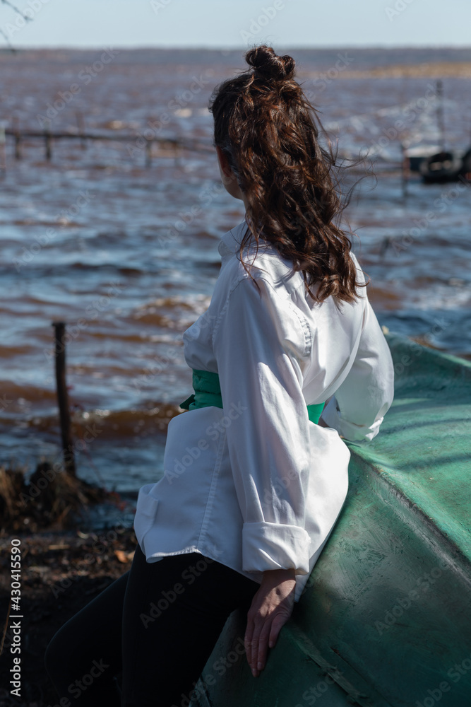 Russian beautiful woman standing back to camera at the lake on a sunny day in a white shirt and green belt. Russian beautiful woman standing back to camera at the lake on a sunny day in a white shirt and green belt.