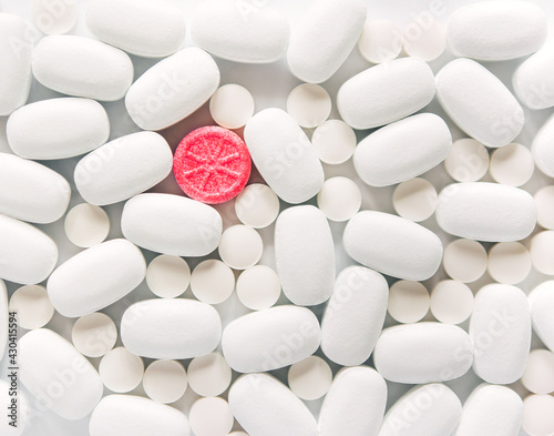 White pills on a white background. One bright pink round pill accent. Oblong and round pills close-up. Healthcare and medicine.