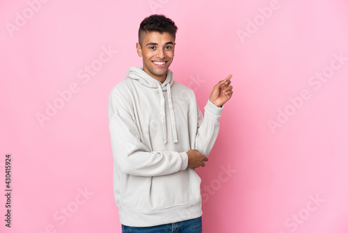 Young Brazilian man isolated on pink background pointing finger to the side © luismolinero