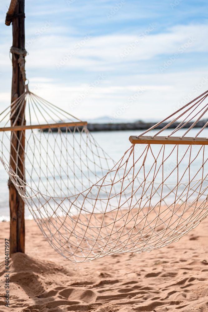 Obraz premium Rope hammock hanging on tropical beach, sea and sky are blurred background.