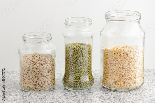 Variety of dry legumes: lentils, peas, green gram in glass jars uncooked on white kitchen background, zero waste, eco friendly, balanced diet food, healthy clean eating, vegan protein concept