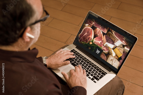 Un signore fa la spesa on-line da casa seduto davanti al suo computer portatile photo