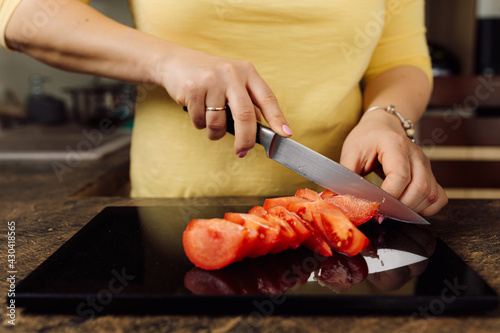 female hands cut a tomato into pieces with a knife on a natural stone cutting board. home care concept. vegan food