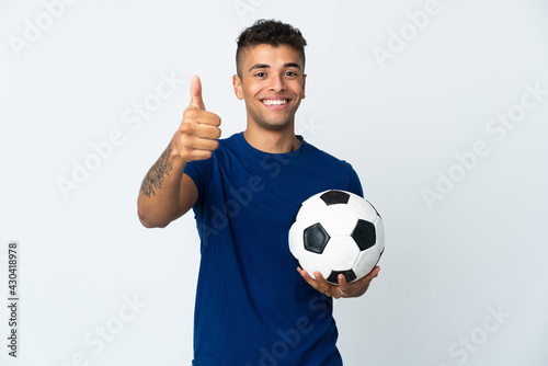 Young Brazilian man over isolated background with soccer ball and with thumb up