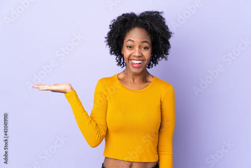 Young African American woman isolated on purple background holding copyspace imaginary on the palm to insert an ad
