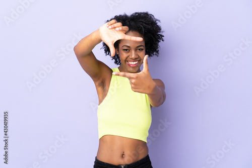 Young African American woman isolated on purple background focusing face. Framing symbol