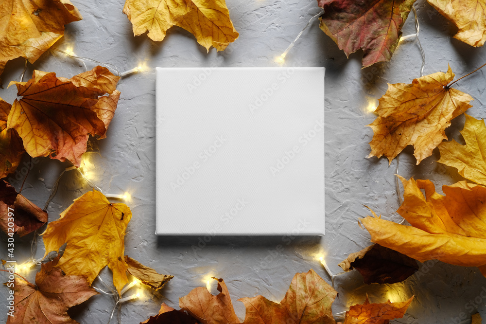 Fototapeta premium Blank canvas frame on autumn background with maple leaves and lights. Mockup poster, autumn concept.