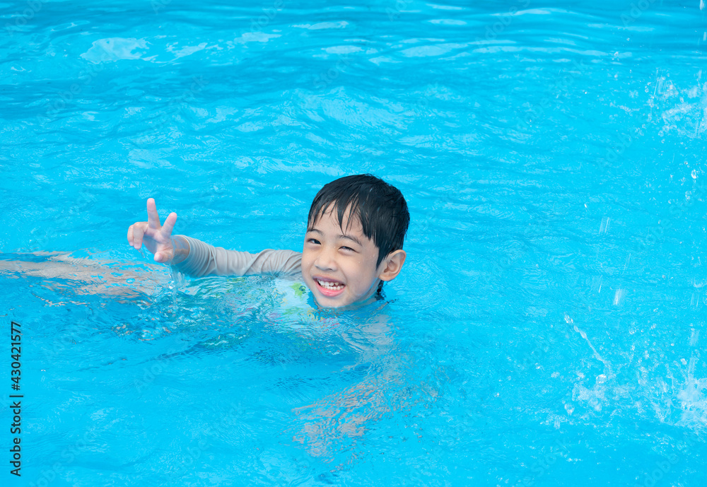 Happy Asian cute boy five years old is swimming and playing in the blue clear swimming pool. He is relaxing during his summer holidays.