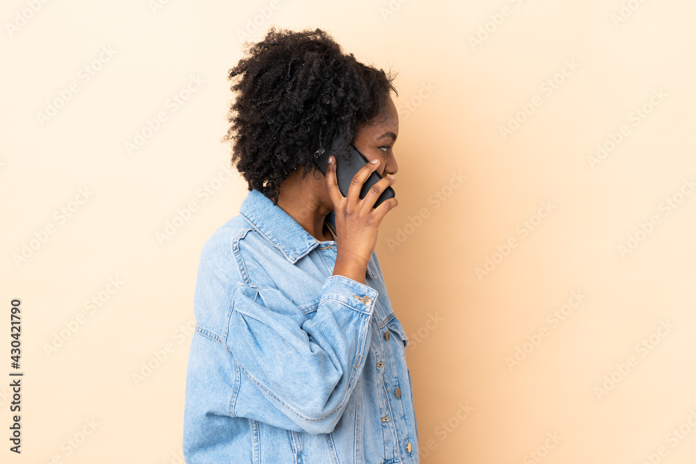 Young African American woman isolated on beige background keeping a conversation with the mobile phone with someone Young African American woman isolated on beige background keeping a conversation with the mobile phone with someone