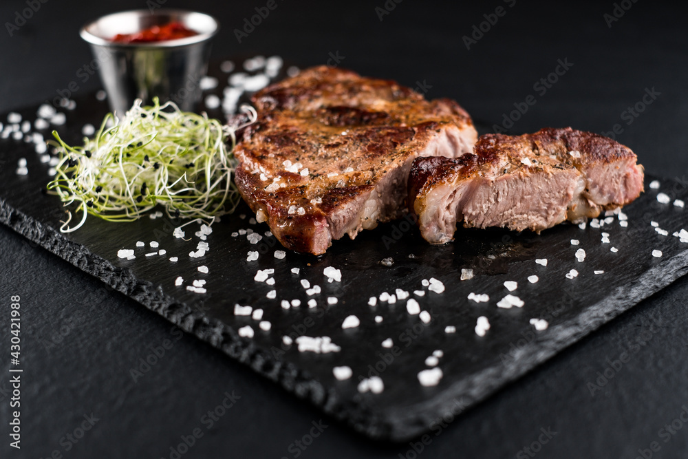 juicy chicken steak with red sauce and herbs on a stone textured plate and black background
