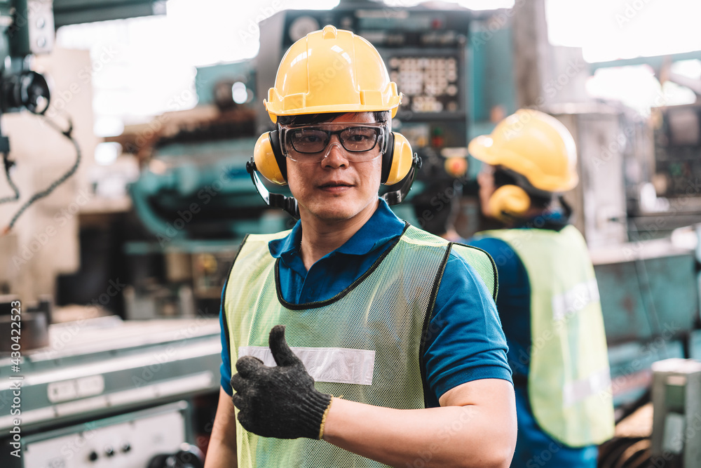 Portrait of Asian worker man  working in safety work wear with yellow helmet and glasses l ear muff l glove.male technician asia is happy looking at camera and show thumbs up in factory industrial