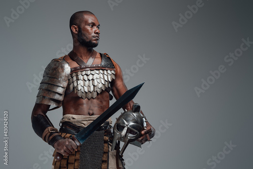 African gladiator with sword against gray background