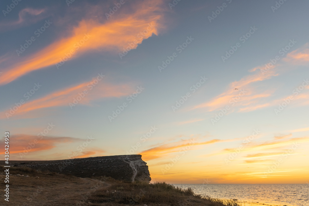 Magnificent sunset on the coast of the Crimean cape Tarkhankut. Orange clouds over a rocky cliff on the Black Sea coast.