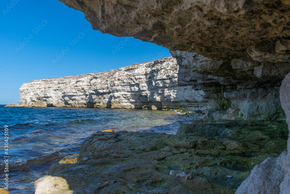 The sheer white cliffs of Cape Tarkhankut on the Crimean Peninsula overhang the waters of the Black Sea. Waves of dark blue, surprisingly rich color roll on the deserted shore of a secluded bay.