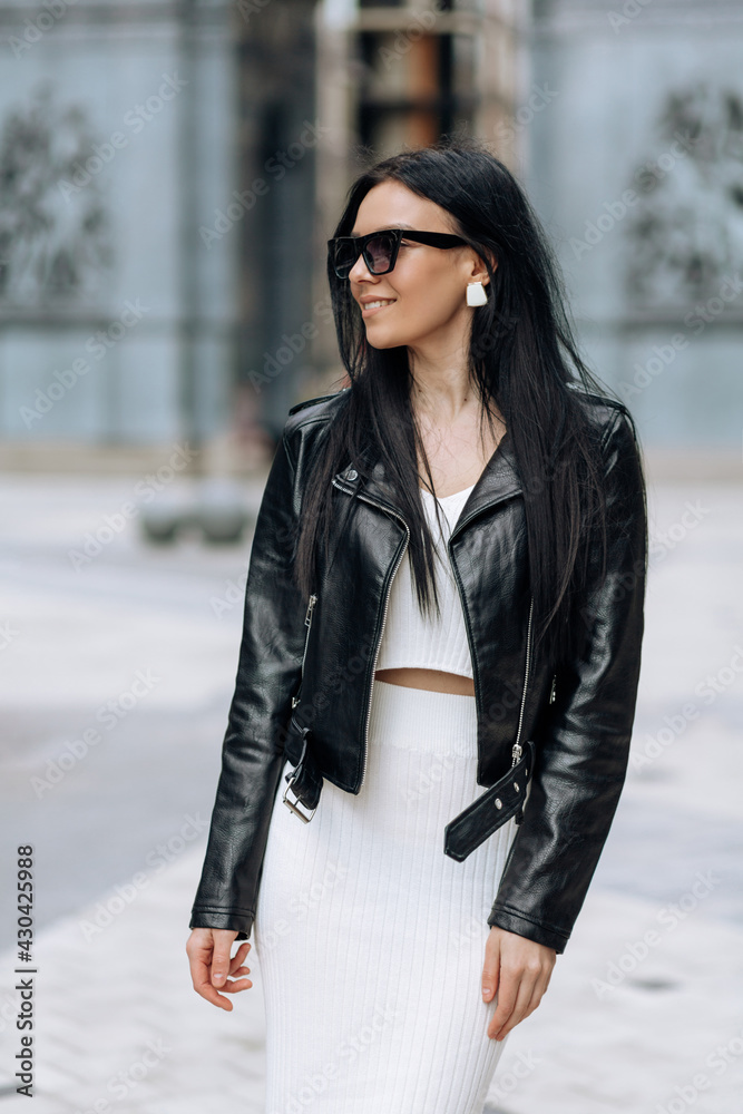 A young beautiful brunette in sunglasses and a fashionable outfit is walking around the city. Smiling portrait