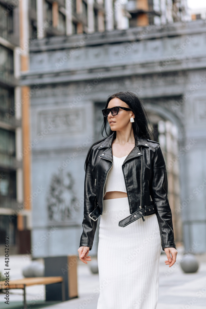 Fototapeta premium Young beautiful brunette in sunglasses and a fashionable outfit walking in the city