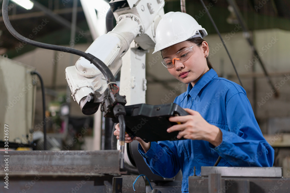 Female engineer checking robotic arm machine for system welding with remote control at a factory Industrial Female engineer checking robotic arm machine for system welding with remote control at a factory Industrial