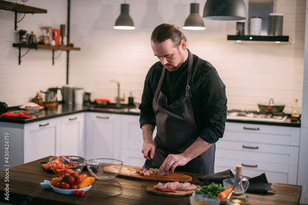 A male chef prepares fresh meat at home in the kitchen..