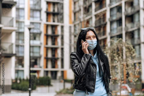 Young brunette girl in a mask from the virus talking on the phone on the street