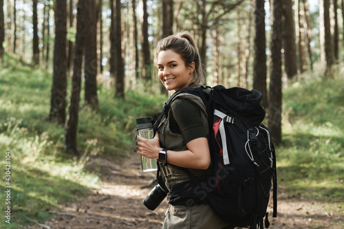 Female hiker with big backpack and reusable bottle for water in green forest
