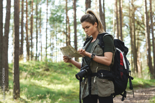 Female hiker with big backpack using map for orienteering in the forest