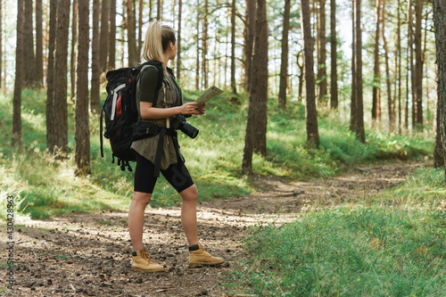Fototapeta Naklejka Na Ścianę i Meble -  Female hiker with big backpack using map for orienteering in the forest